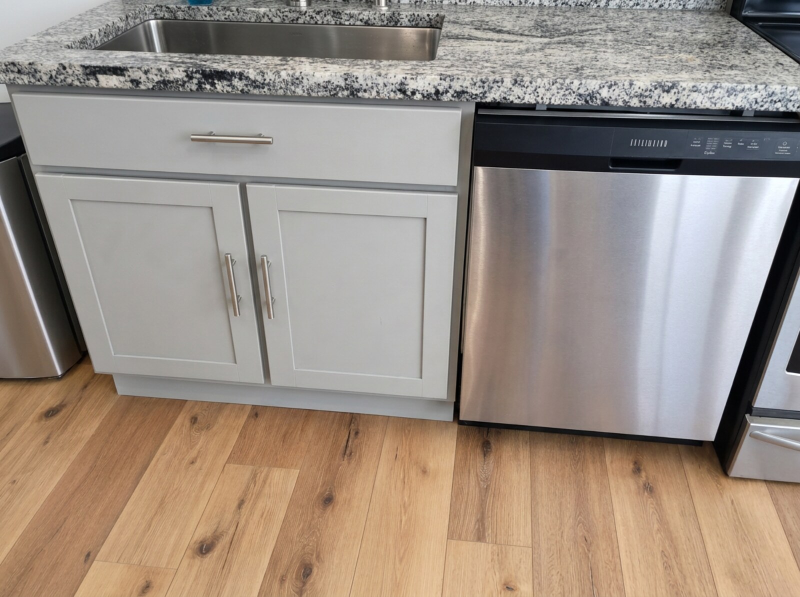 Gray painted sink base cabinet with granite countertop and built-in stainless dishwasher after refinishing