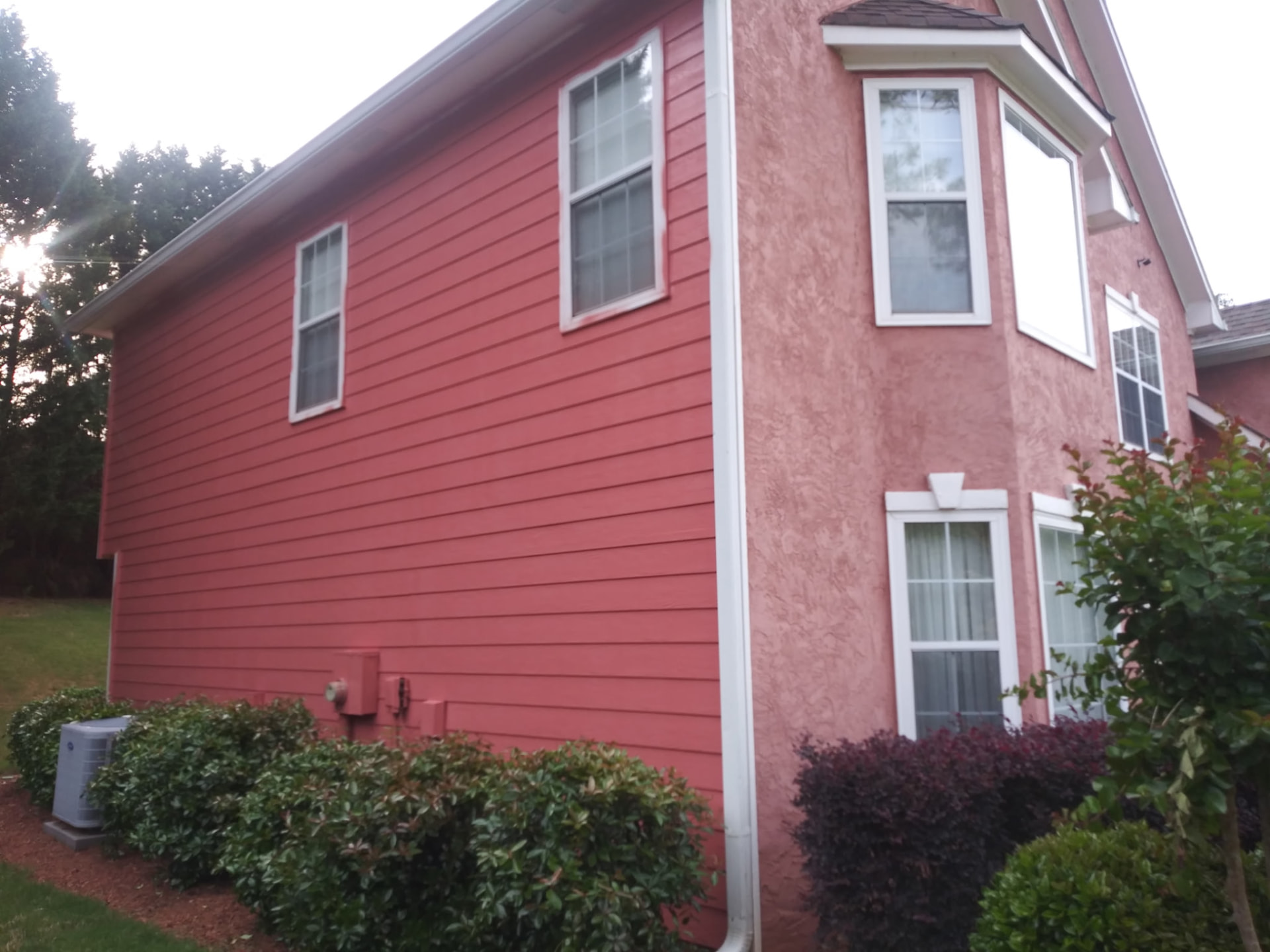 Exterior painting detail of red siding, stucco accent wall and fresh window trim