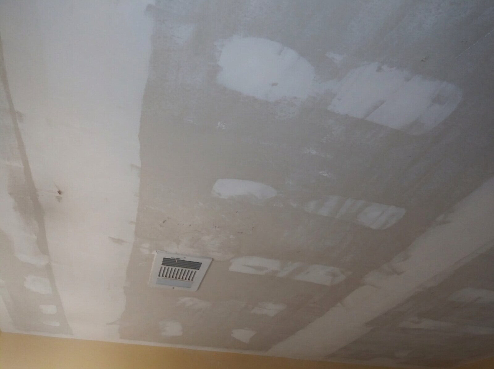 The same room with new sheetrock installed on the ceiling, taped seams and joint compound patches, and a ceiling air register, before texture and paint