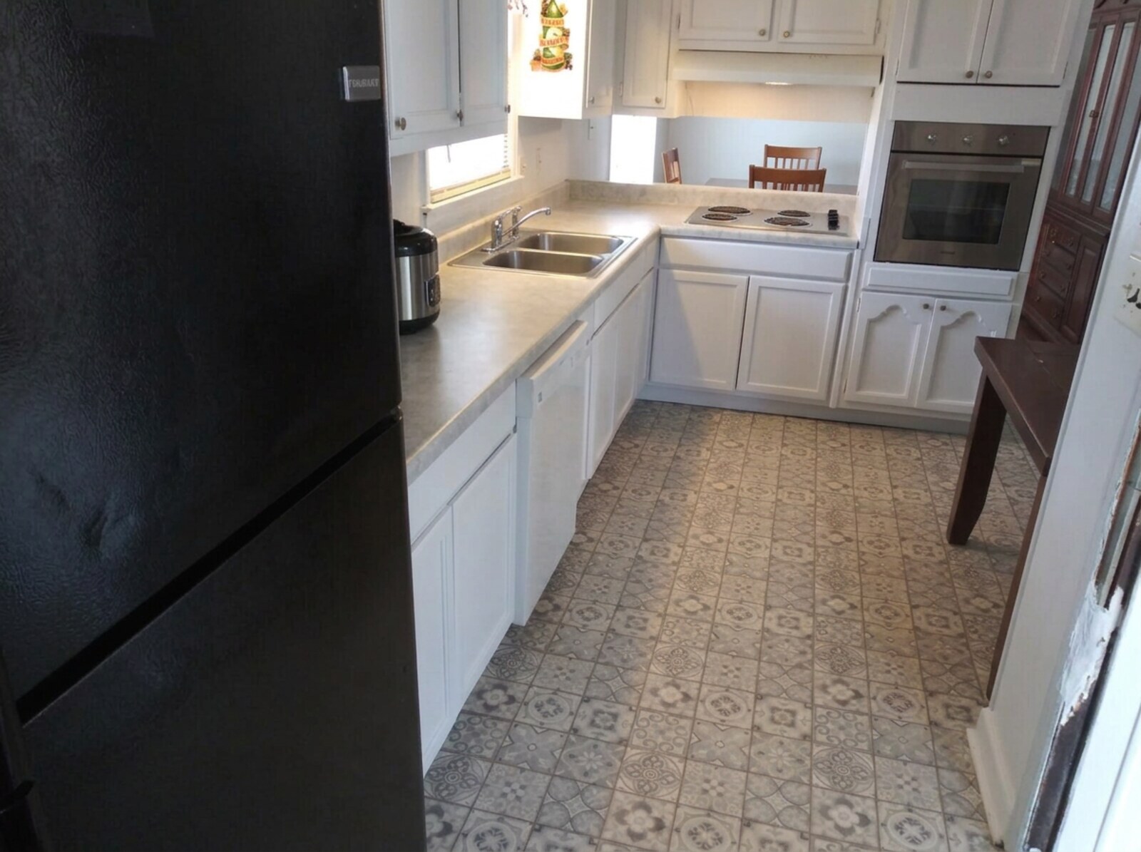Finished kitchen with white painted cabinets, light laminate countertops, black refrigerator, cooktop under a white range hood and a stainless built-in wall oven