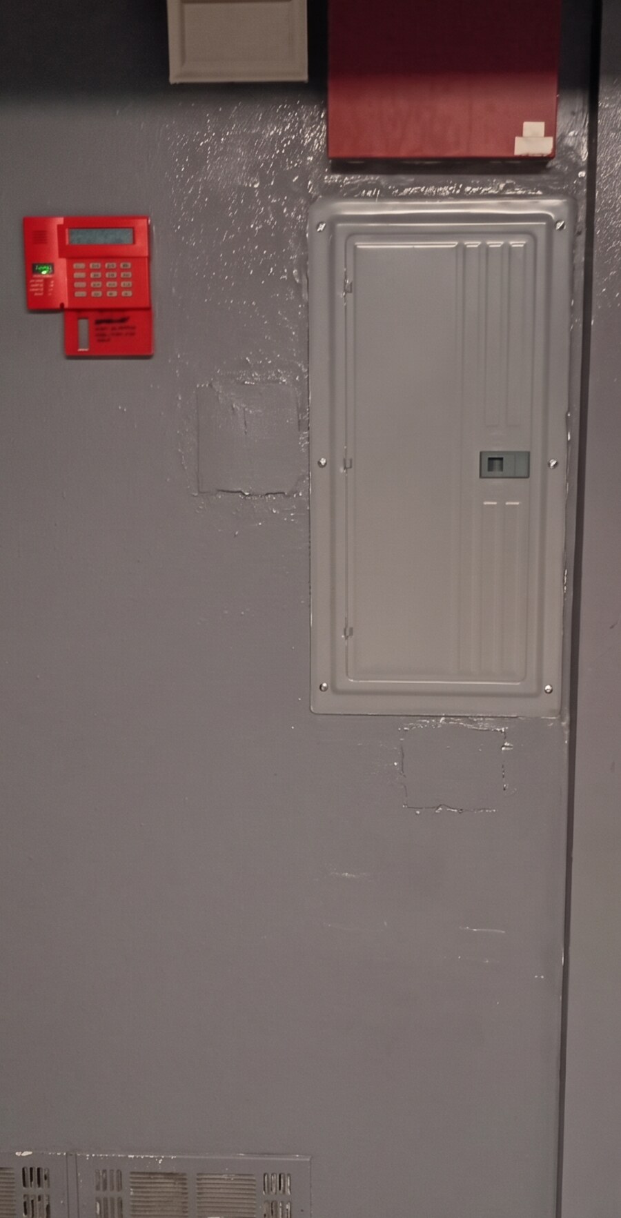 The same wall patched, textured and painted to match the surrounding gray paint, with the breaker panel refitted