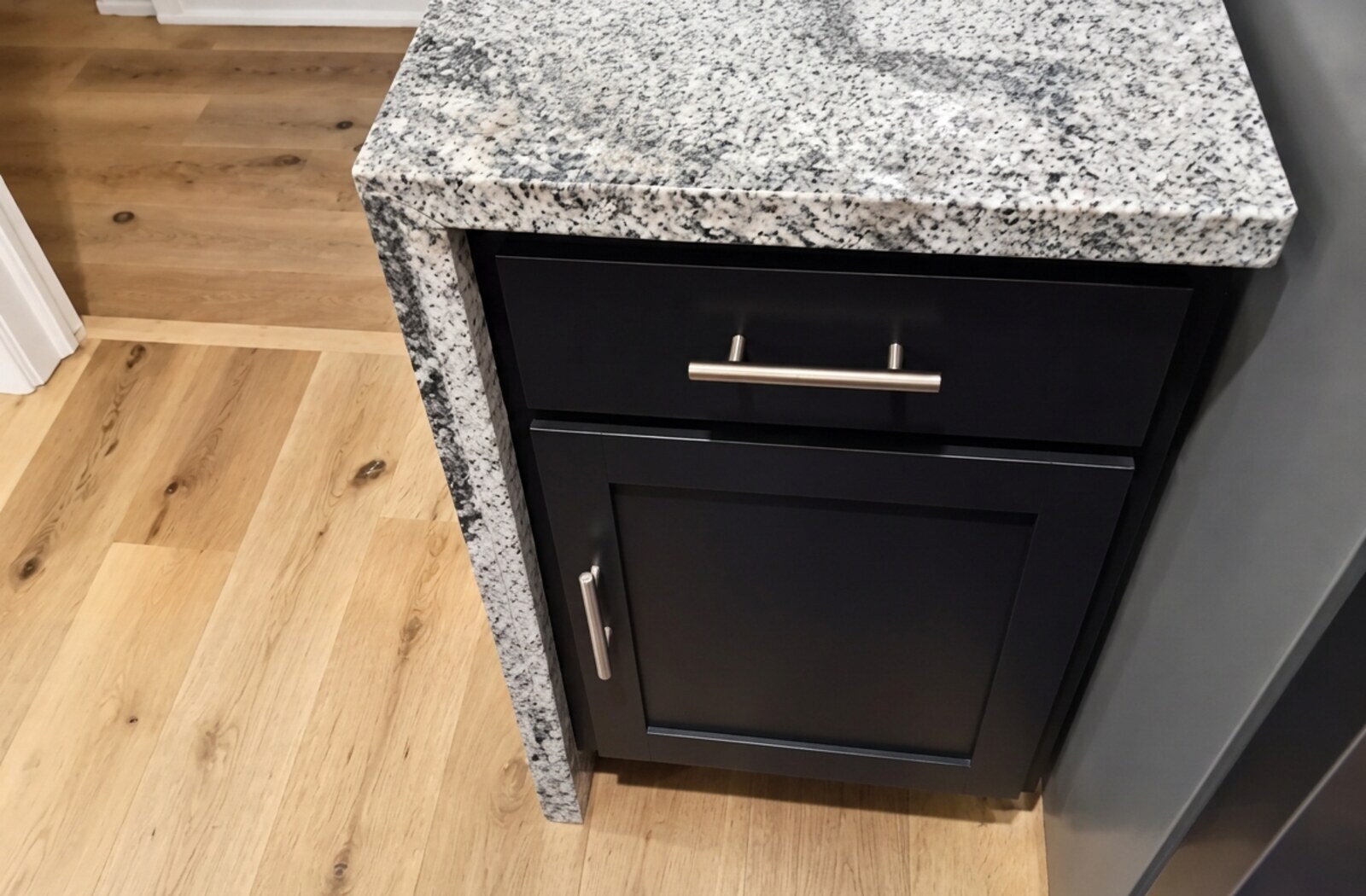 Black shaker base cabinet with speckled granite waterfall countertop before being refinished gray