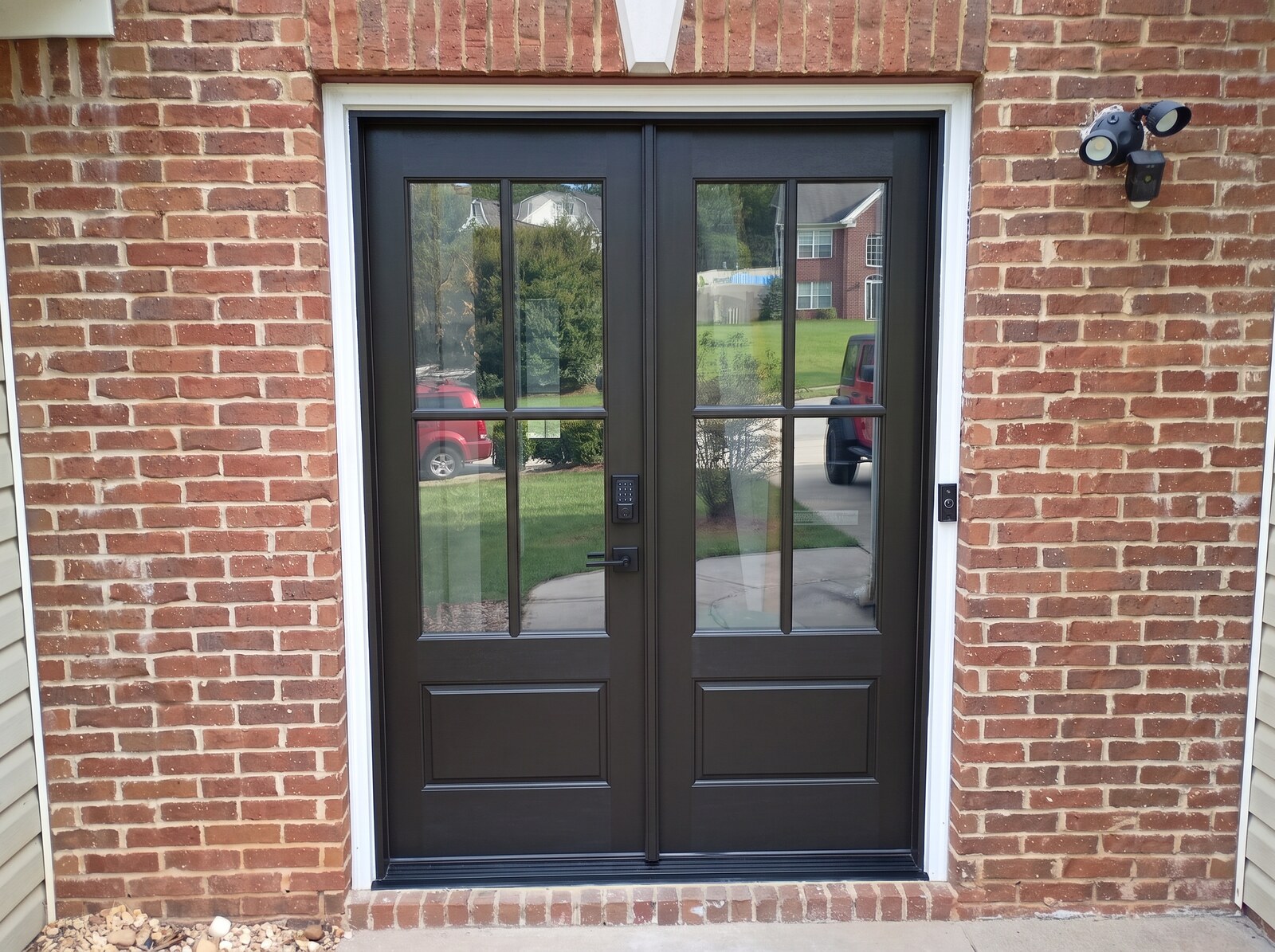 The same front entry fitted with dark bronze double French doors with divided glass panels and a black keypad deadbolt