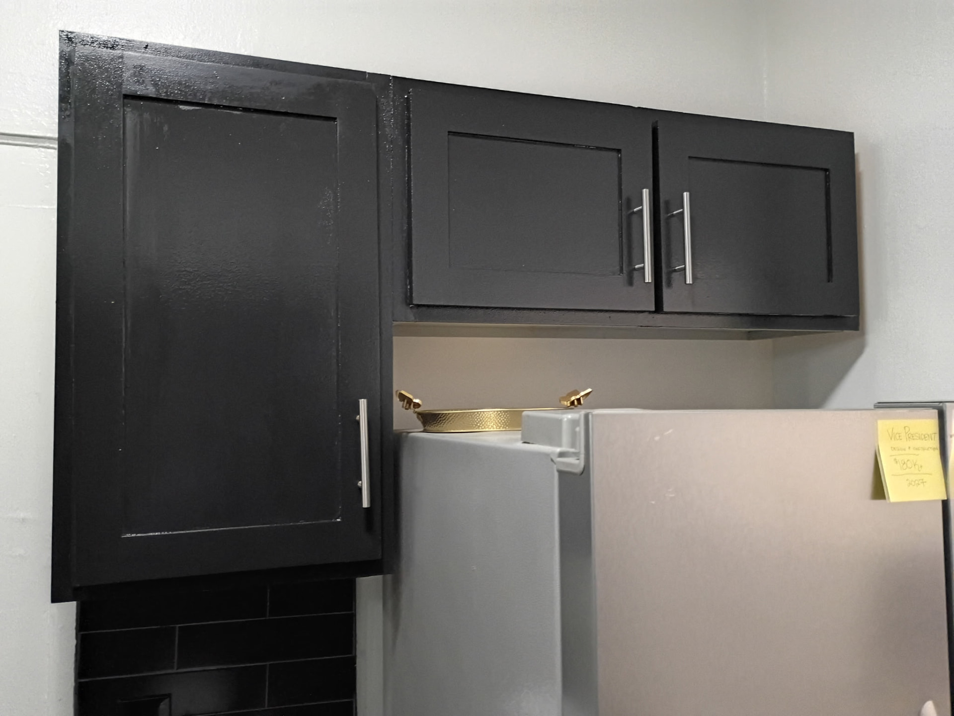 Black painted upper cabinets beside a stainless refrigerator before being refinished gray