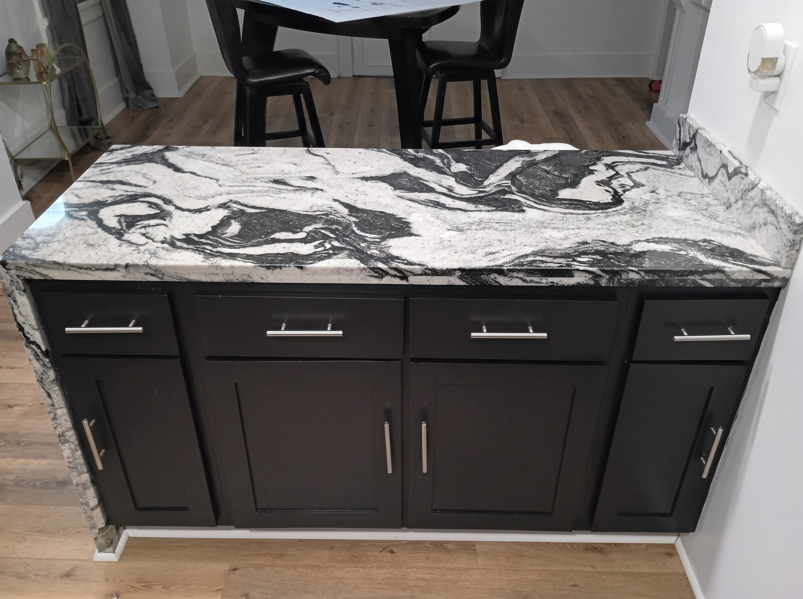 Kitchen island with black shaker cabinets, silver bar handles and veined granite countertop before being painted gray