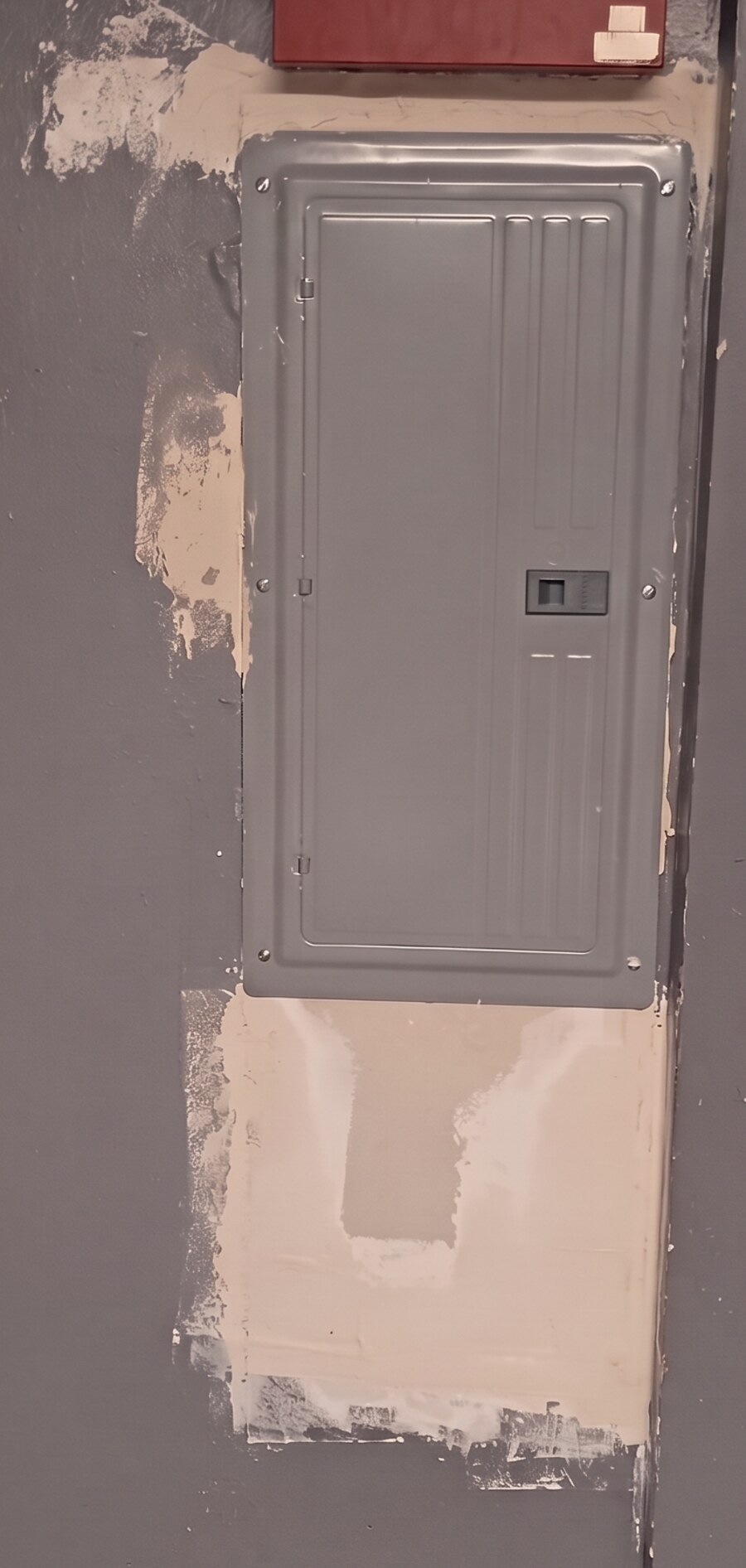 The same wall with new drywall fitted below and around the breaker panel and coated with joint compound, before paint