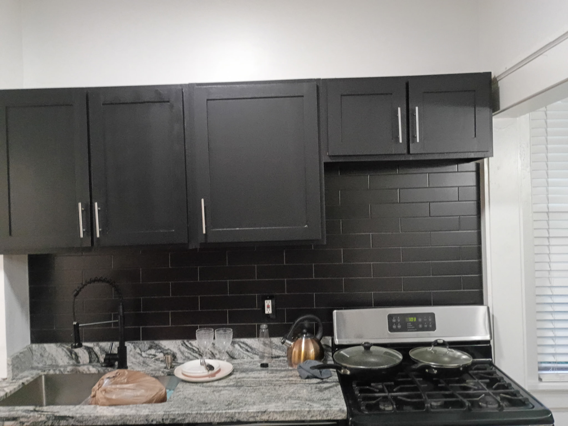 Bank of black upper cabinets with black subway tile and granite counters before being refinished gray