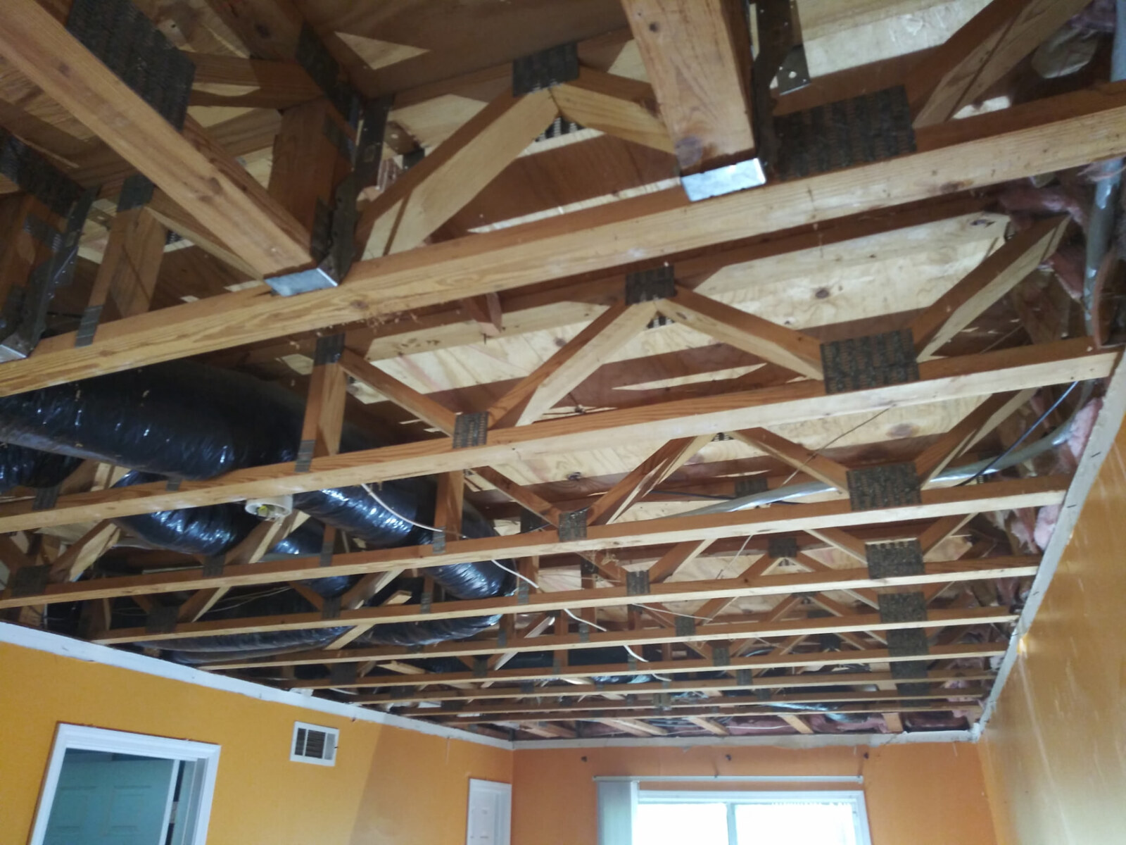 Room with yellow walls and the ceiling open to exposed wood roof trusses, ductwork and wiring before new sheetrock was installed